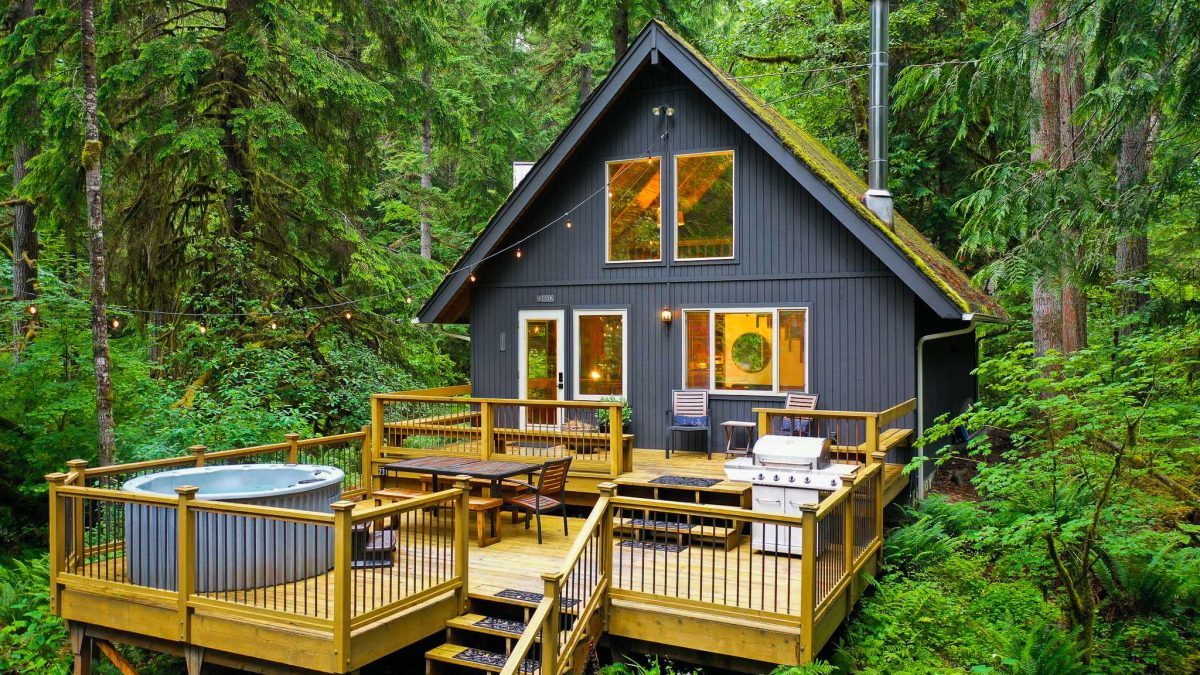 A hot tub on the deck of an A-frame cabin in the forest