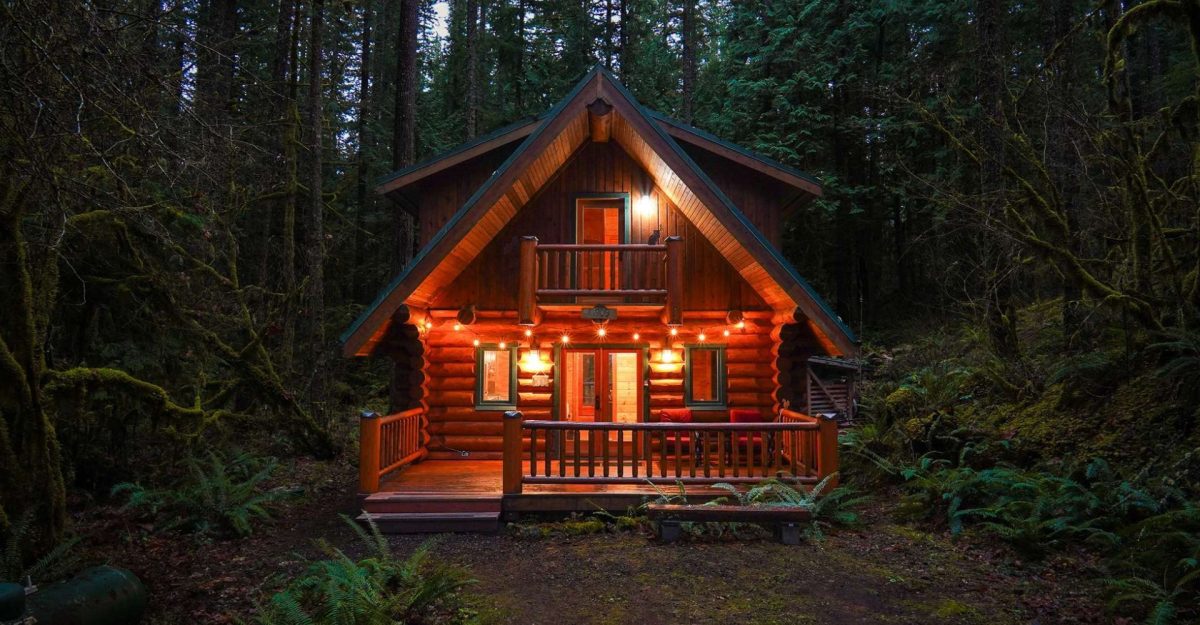 A log cabin lit at dusk among the evergreens in Snowline